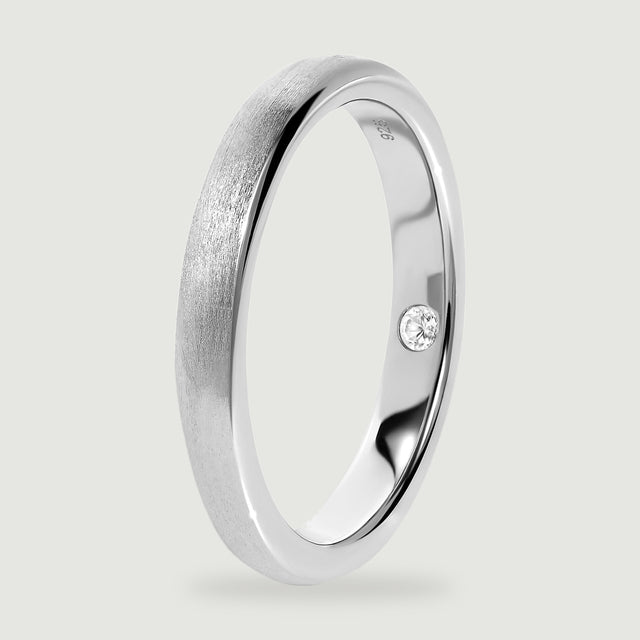 An upright silver ring reveals the smooth inner band, rounded rim, and inset clear stone.