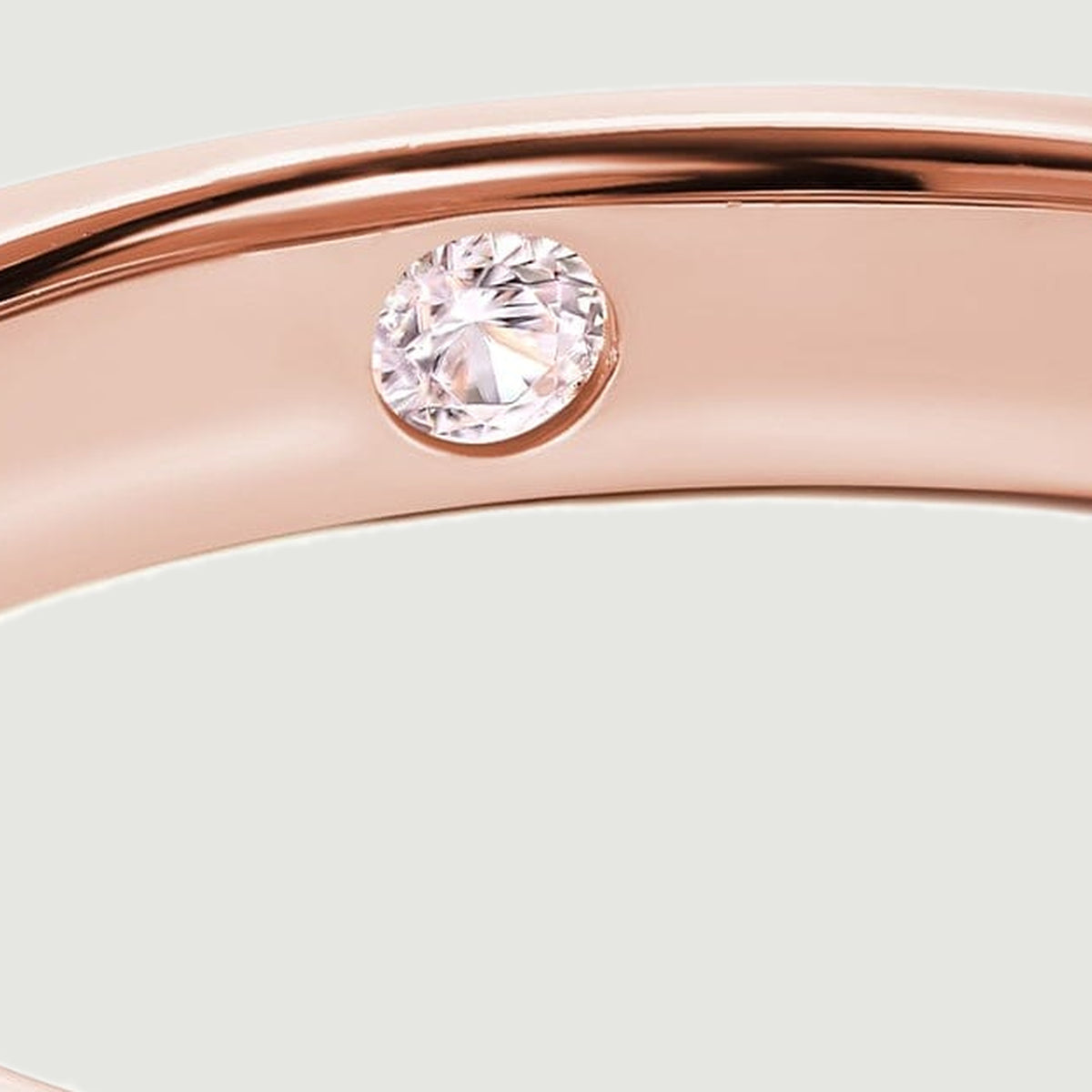 A clear round stone sits flush inside the rose gold band beside the bright polished rim.