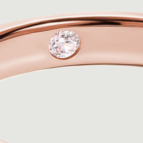 A clear round stone sits flush inside the rose gold band beside the bright polished rim.