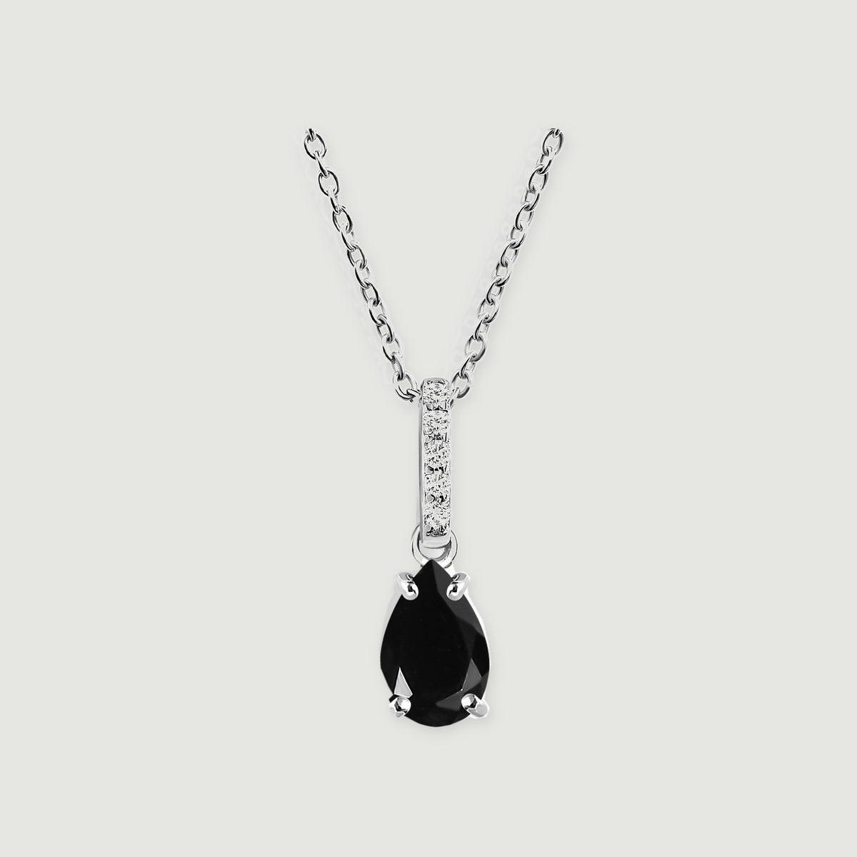 A sterling silver chain holds a pear-shaped black onyx pendant beneath a row of clear stones on a pale gray background.
