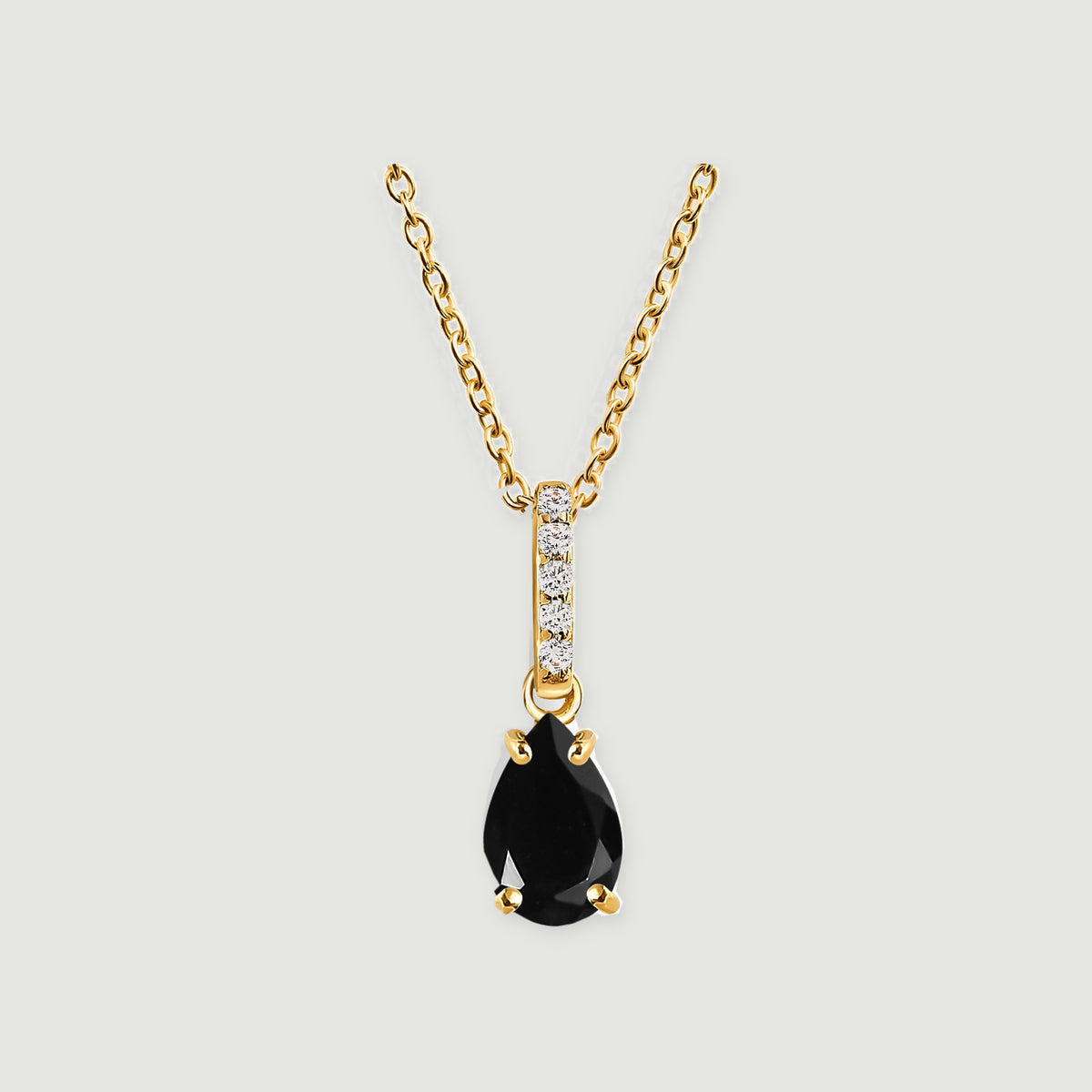 A yellow gold vermeil chain and four-prong black onyx pendant are centered against a light gray surface.