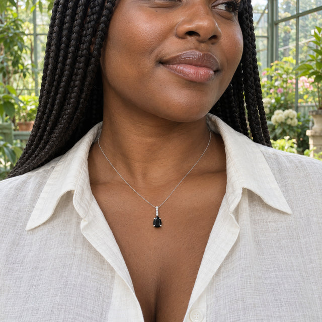 A woman with long braids wears a sterling silver black onyx necklace with an ivory linen shirt in a leafy conservatory.