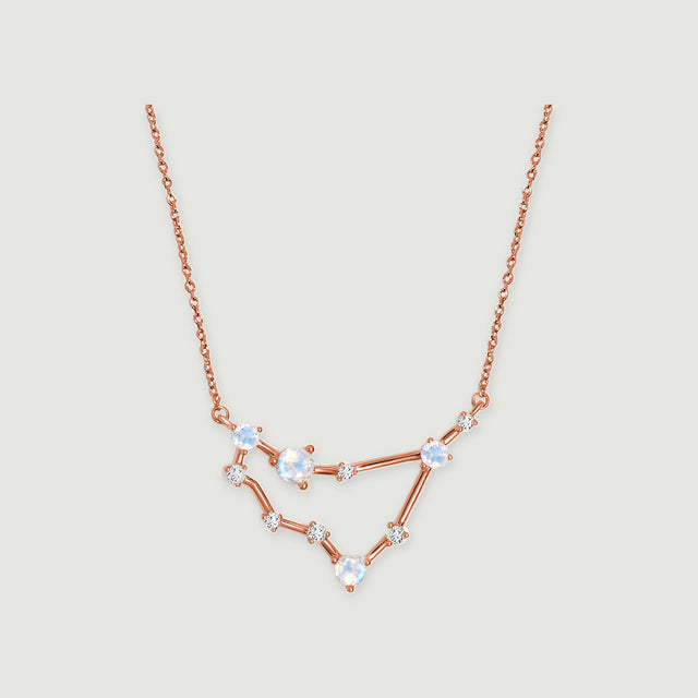 A rose gold necklace shows a fine chain and an angular arrangement of round stones on a light gray surface.