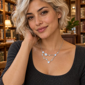A woman with short pale hair wears the silver necklace above a charcoal neckline in a bookshop.