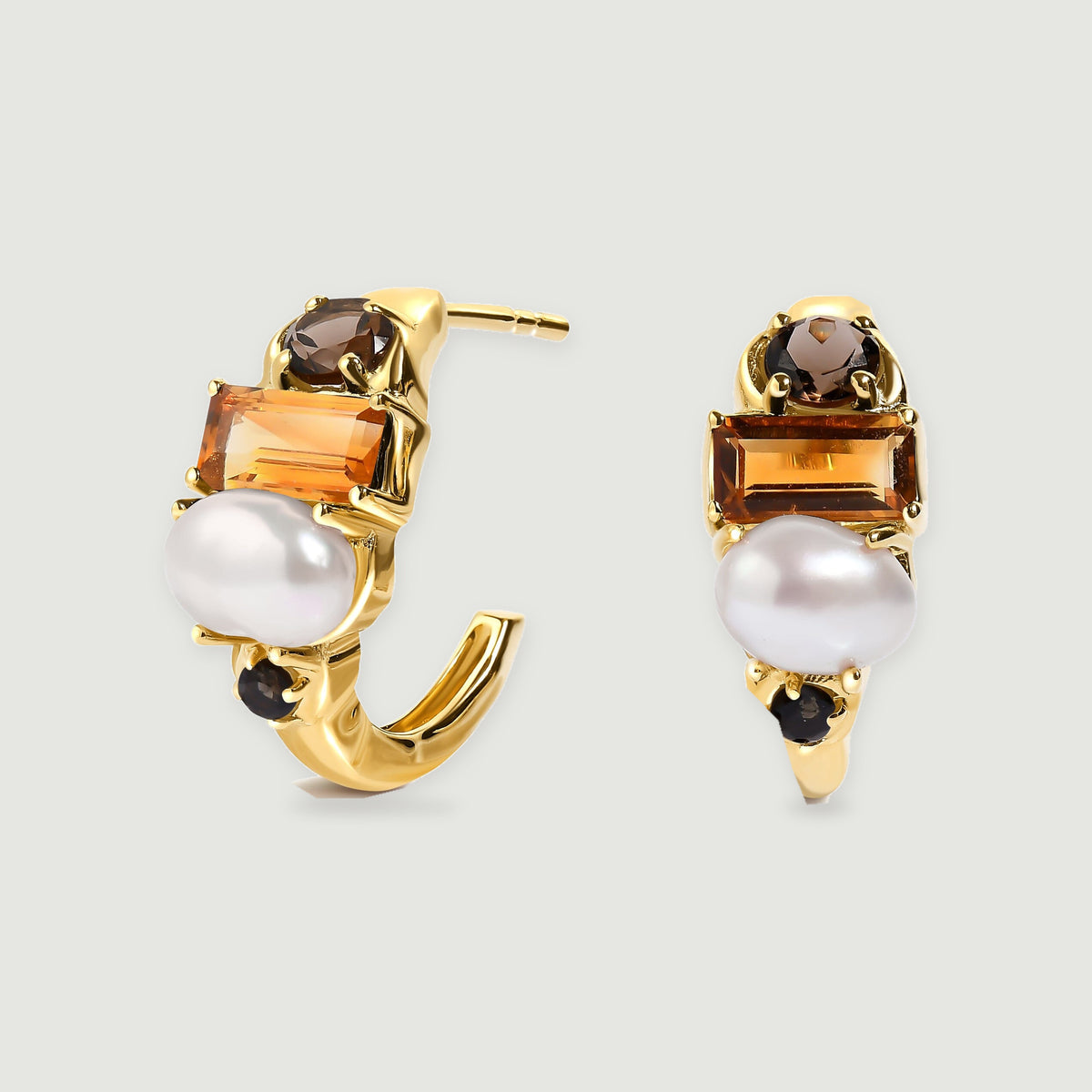 Two gold-tone hoop earrings display rectangular amber stones, white pearls, and small dark round stones on a light gray surface.
