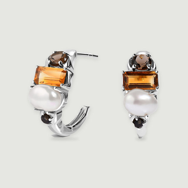 A pair of silver-tone hoops with white pearls and orange rectangular stones stands against a light gray background.