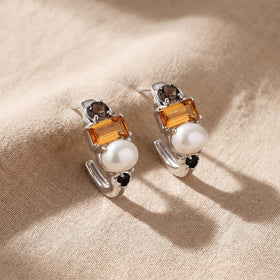 Silver-tone earrings lie side by side on beige cloth with their orange stones and white pearls facing upward.