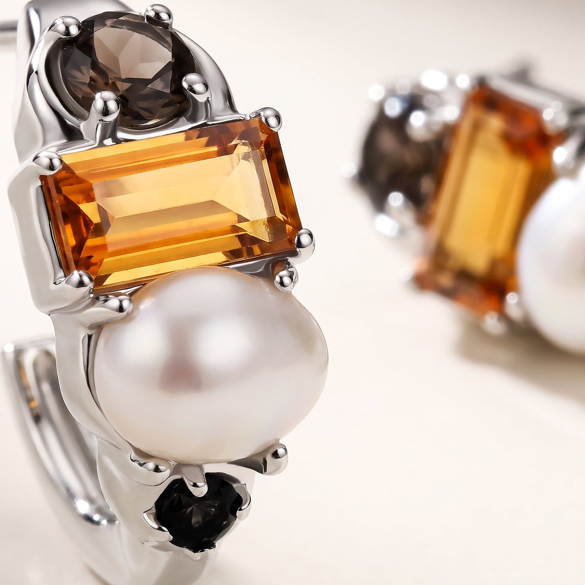 Polished silver-tone prongs surround an orange faceted stone above a white pearl in this close-up.