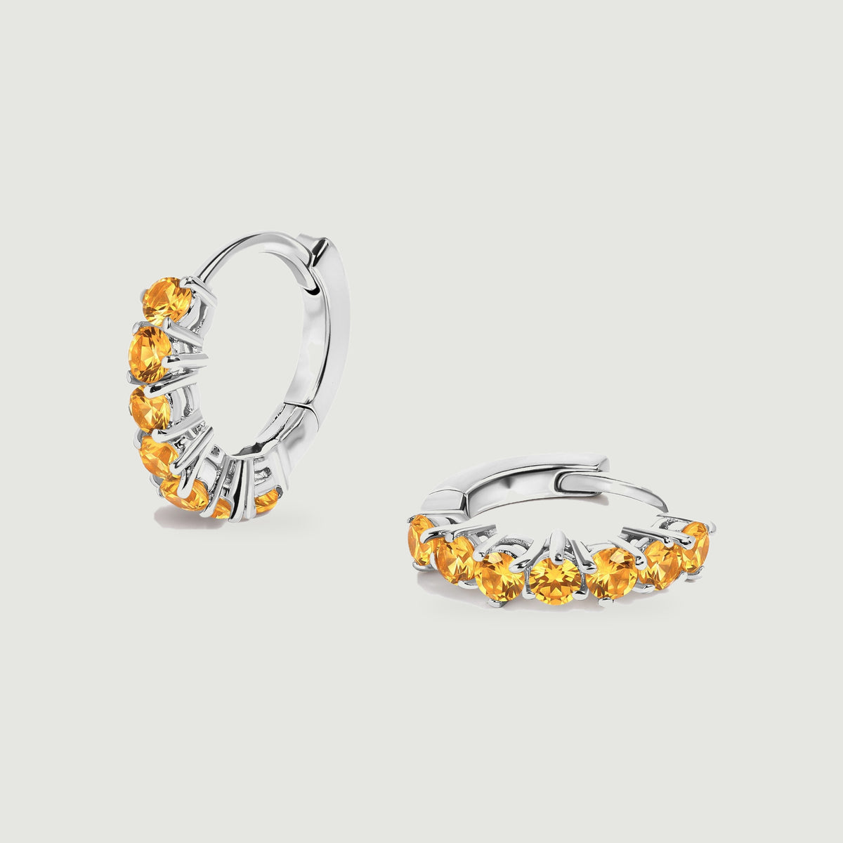 A silver-tone citrine hoop pair rests on a pale gray surface with one earring standing upright.
