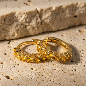 Two gold-tone citrine hoops lie together on a textured beige stone tabletop.