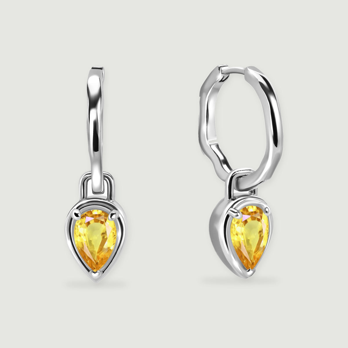 Two white rhodium plated hoops hold faceted pear-shaped citrine drops on a pale gray surface.