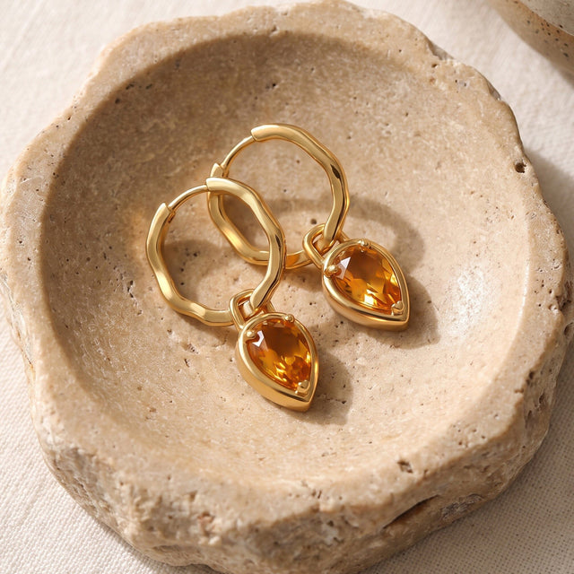Yellow gold plated citrine hoop earrings lie together in a textured beige stone dish.