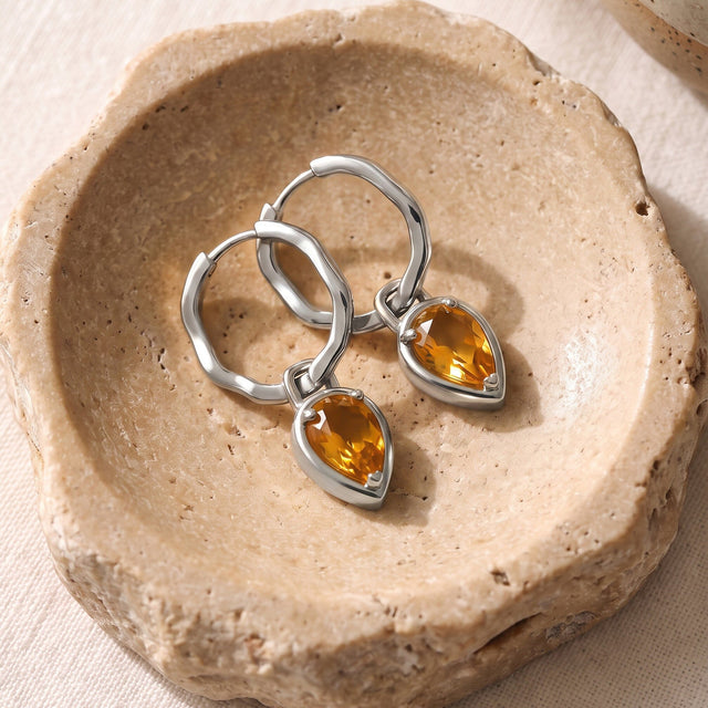 White rhodium plated hoops and amber citrine drops are arranged on a warm stone dish.