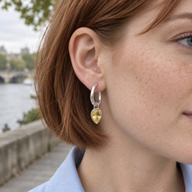 A woman with an auburn bob wears a white rhodium plated citrine hoop beside a riverside walkway.