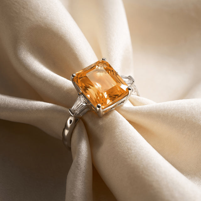 A silver citrine ring rests on cream satin with its textured band and clear side stones visible.