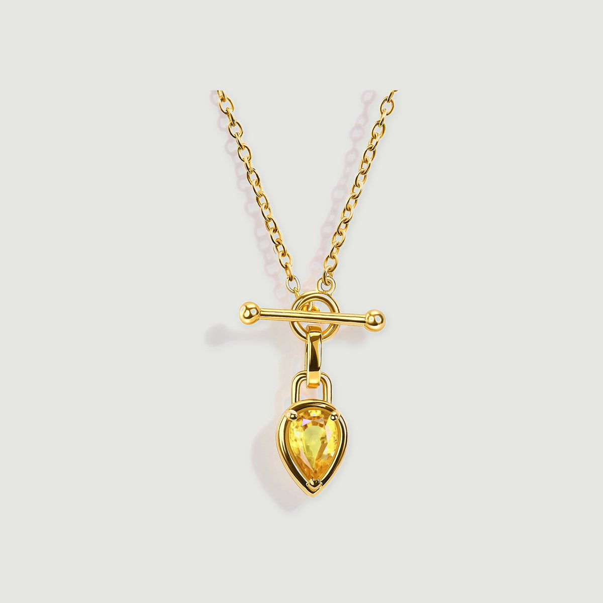 A yellow gold plated chain carries a yellow pear shaped gemstone below a polished horizontal bar.