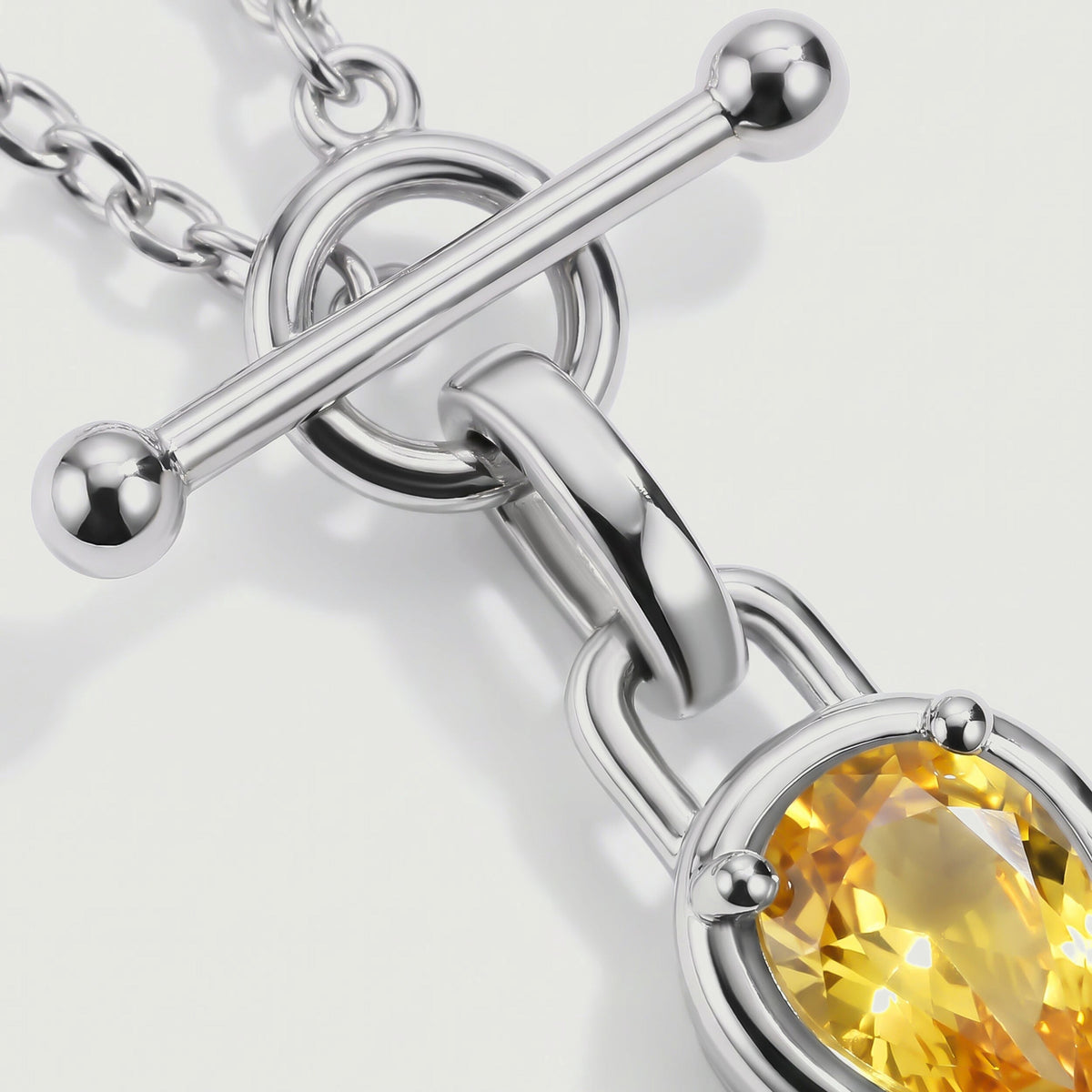 The silver toned rounded bar and curved pendant bail are shown beside the yellow gemstone.