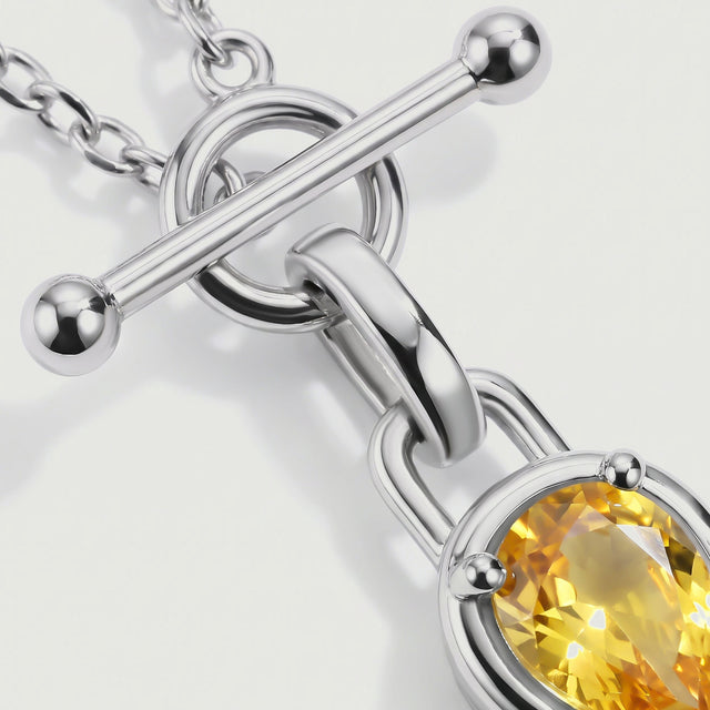 The silver toned rounded bar and curved pendant bail are shown beside the yellow gemstone.