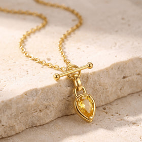 The gold toned necklace drapes across pale textured stone with the yellow pendant resting at the edge.