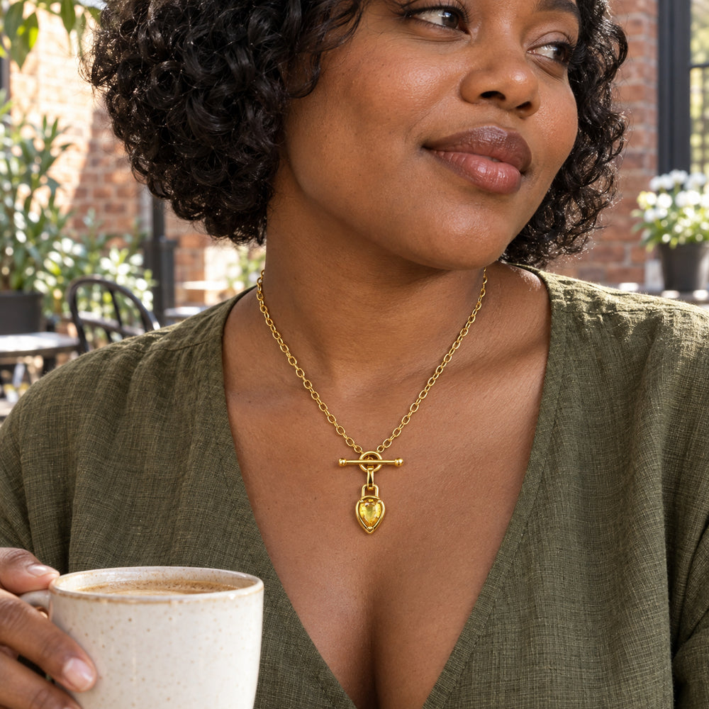 A woman in an olive blouse wears the gold toned citrine necklace while holding a ceramic cup in a brick courtyard.