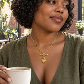 A woman in an olive blouse wears the gold toned citrine necklace while holding a ceramic cup in a brick courtyard.