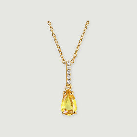 A yellow gold necklace has a pear-shaped yellow gemstone below a straight row of five clear stones.