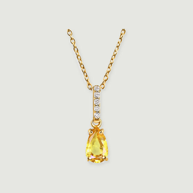 A yellow gold necklace has a pear-shaped yellow gemstone below a straight row of five clear stones.