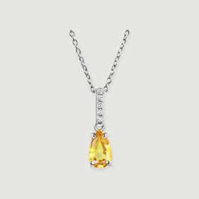 A silver necklace displays a yellow pear-shaped pendant beneath five round clear stones on a pale gray background.