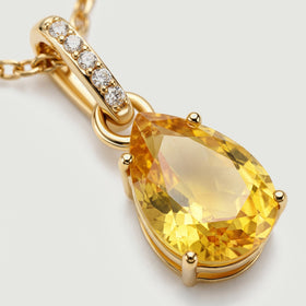 A close view shows the faceted yellow gemstone, polished gold prongs, and five clear stones along the bail.