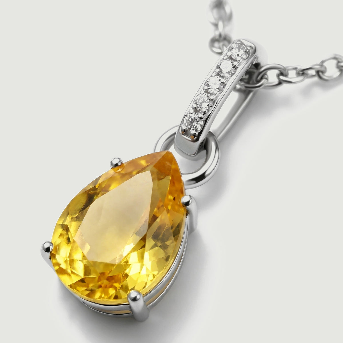 The angled silver pendant reveals rounded prongs, a faceted yellow stone, and the clear stones on its bail.