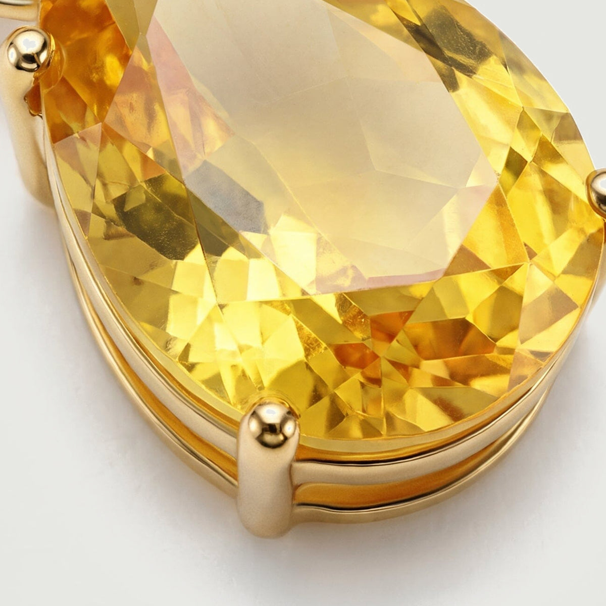 The yellow gemstone shows crisp facets and rounded gold prongs above the edge of its polished setting.