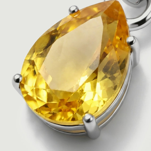 A close view reveals the yellow pear-shaped stone held by rounded silver prongs above a curved setting rim.