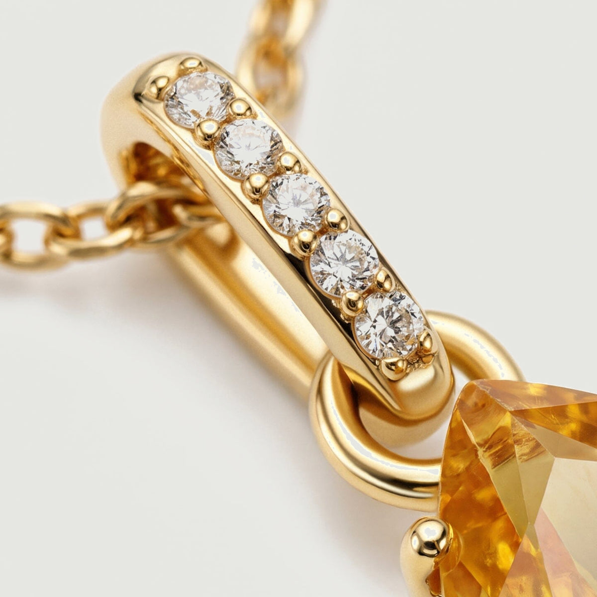 Five round clear stones sit in gold prongs along the narrow bail above the circular pendant connector.