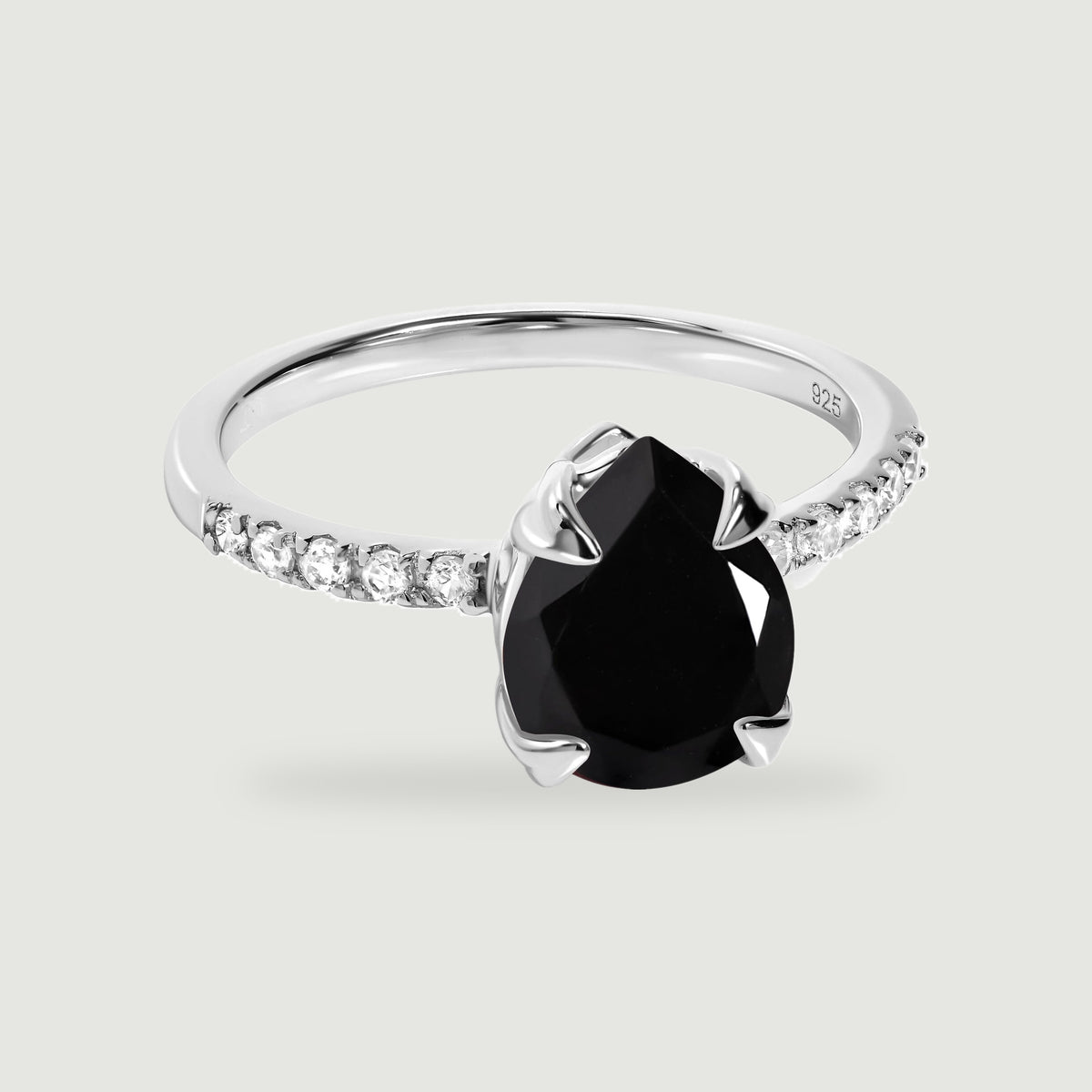 A sterling silver ring with a faceted pear-shaped black stone and clear shoulder stones is centered on a light gray surface.