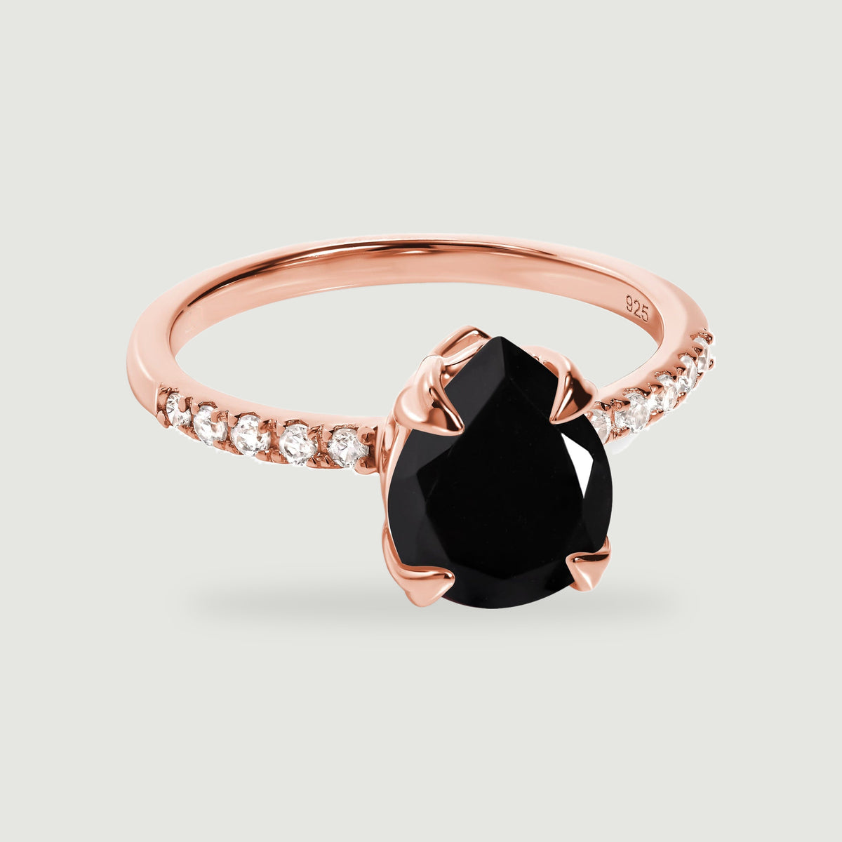 A rose gold vermeil ring with a dark faceted pear-shaped center and four polished prongs rests on a pale gray background.