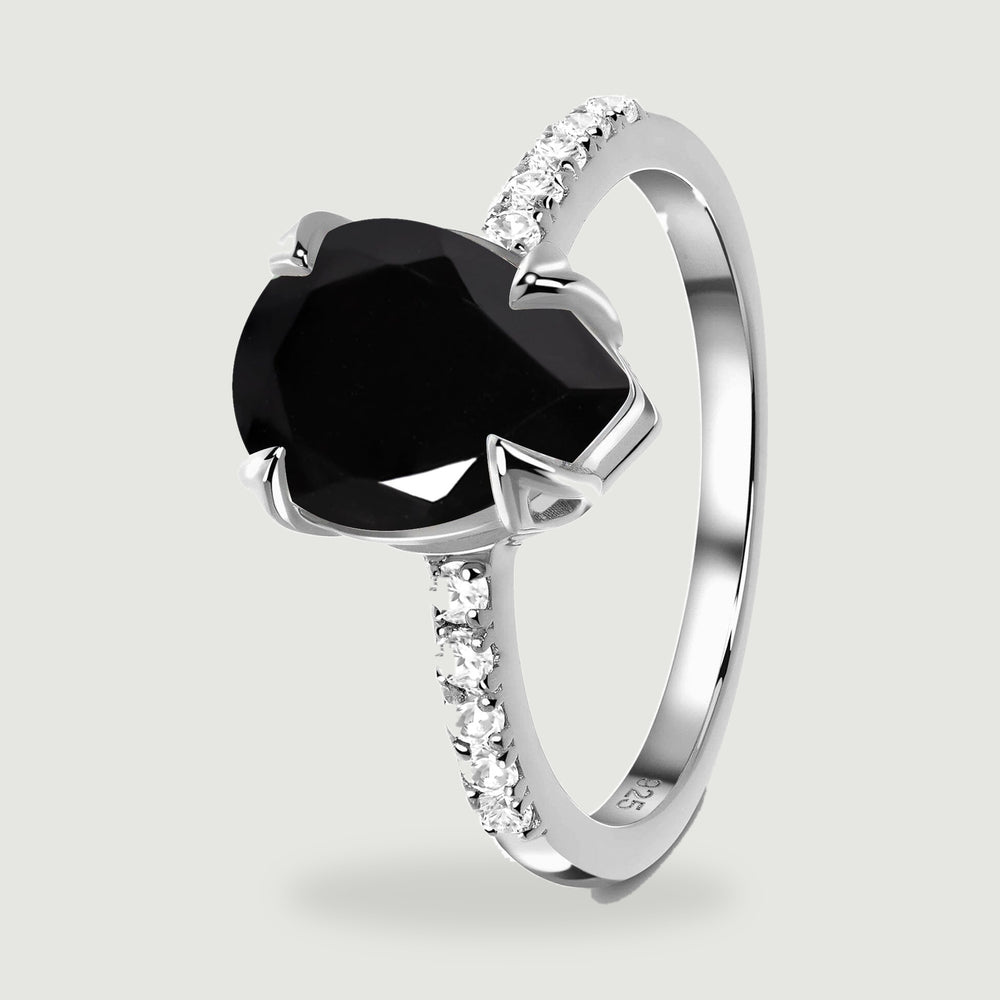 An angled view of a sterling silver ring shows the black stone, raised prongs and clear stones along both shoulders.