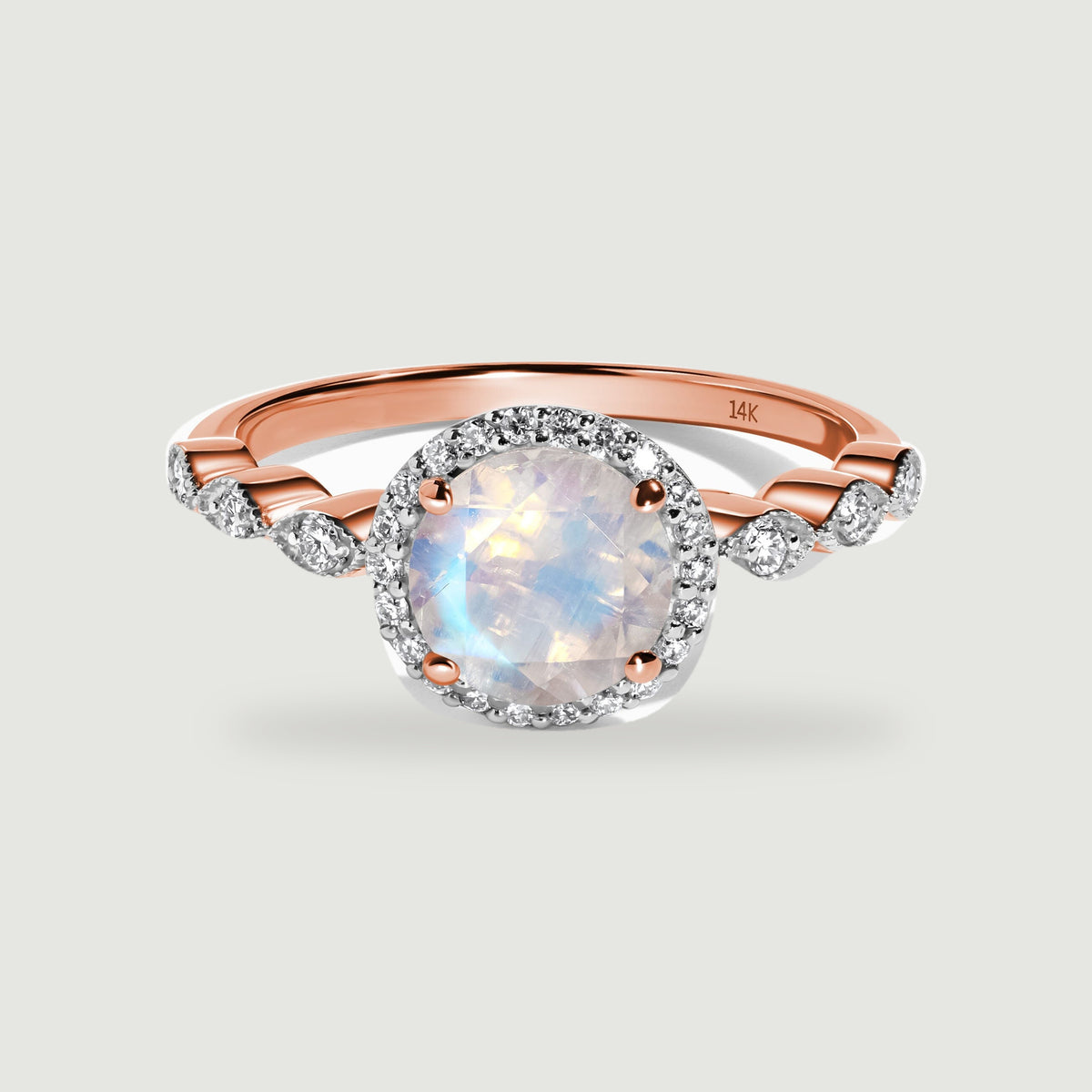 A rose gold ring shows a luminous round moonstone framed by a diamond halo above curved diamond shoulders.
