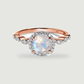 A rose gold ring shows a luminous round moonstone framed by a diamond halo above curved diamond shoulders.