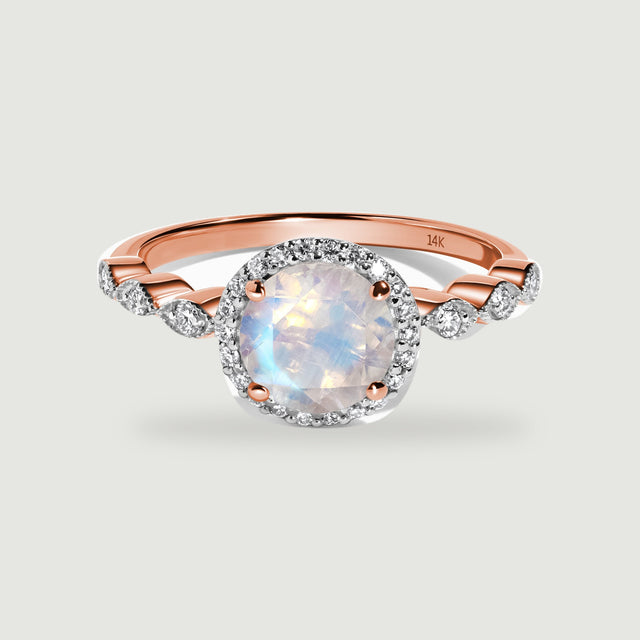 A rose gold ring shows a luminous round moonstone framed by a diamond halo above curved diamond shoulders.