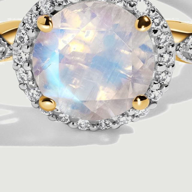 A close view shows yellow gold prongs around a rainbow moonstone with a ring of small clear diamonds.
