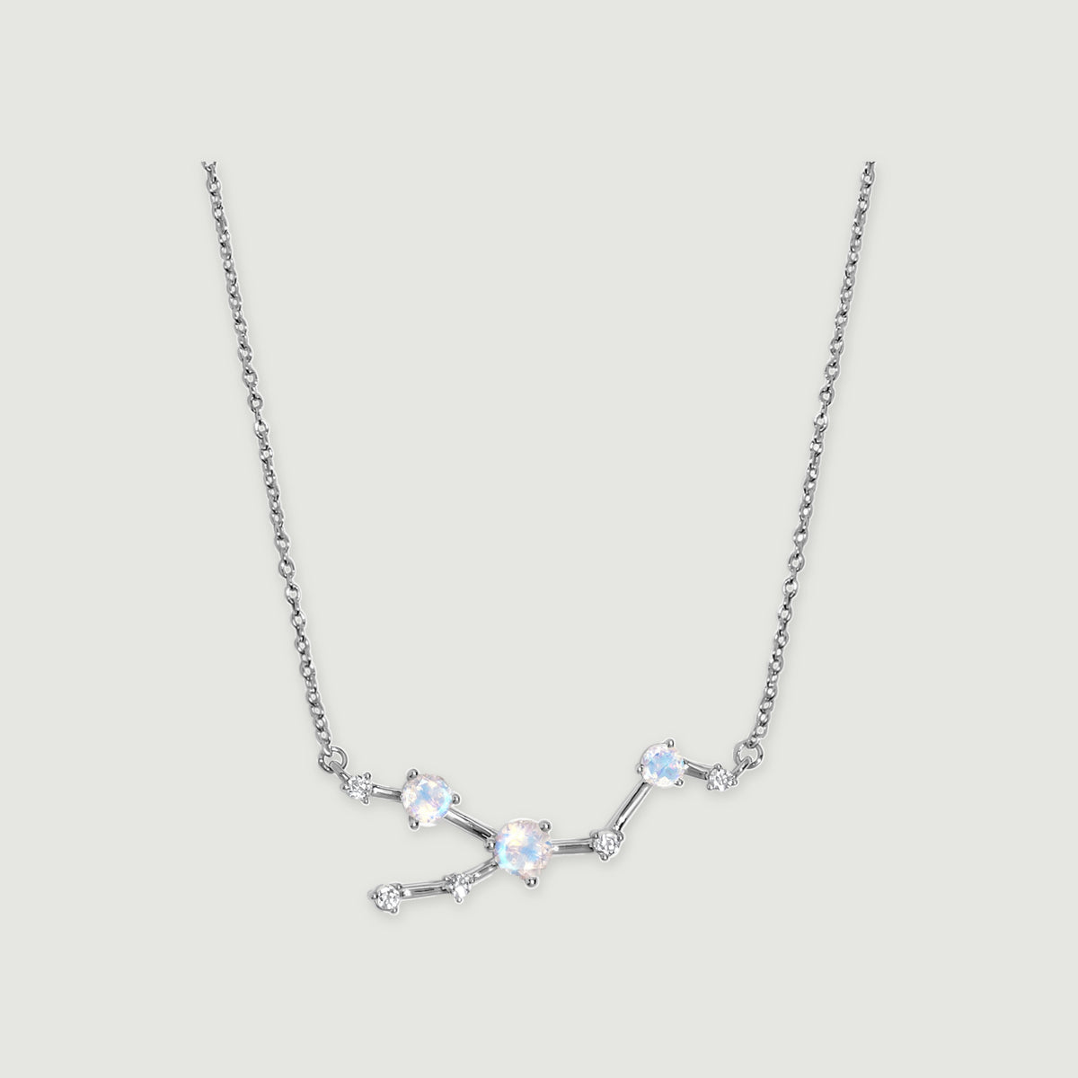 A silver necklace displays an asymmetric arrangement of round iridescent stones and small clear accents.