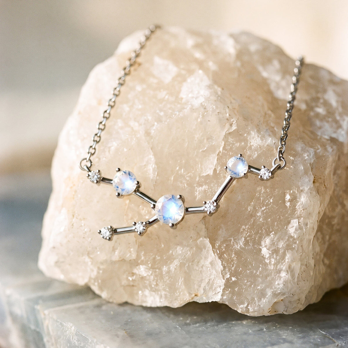 A silver chain and branching stone arrangement rest against a pale textured crystal on a gray slab.