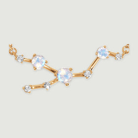 Three iridescent stones and five clear accents form a branching yellow gold centerpiece on a light gray surface.