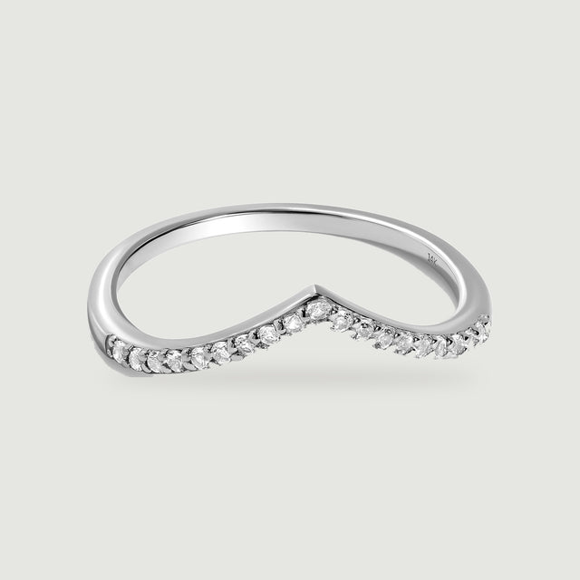 A white gold chevron ring with round diamonds is centered on a pale gray surface.