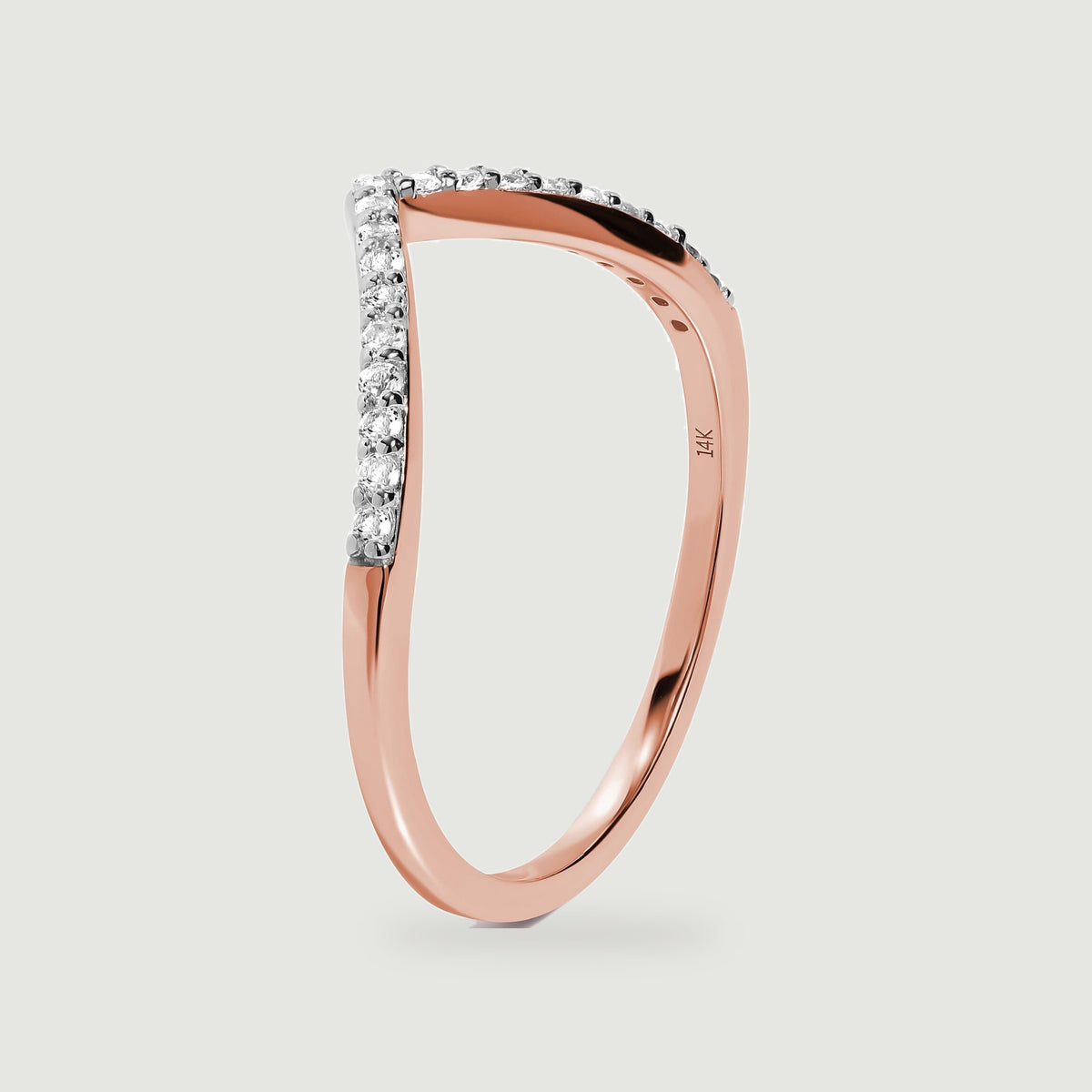 A rose gold ring stands on its edge, showing the curved shank and diamond-lined front.