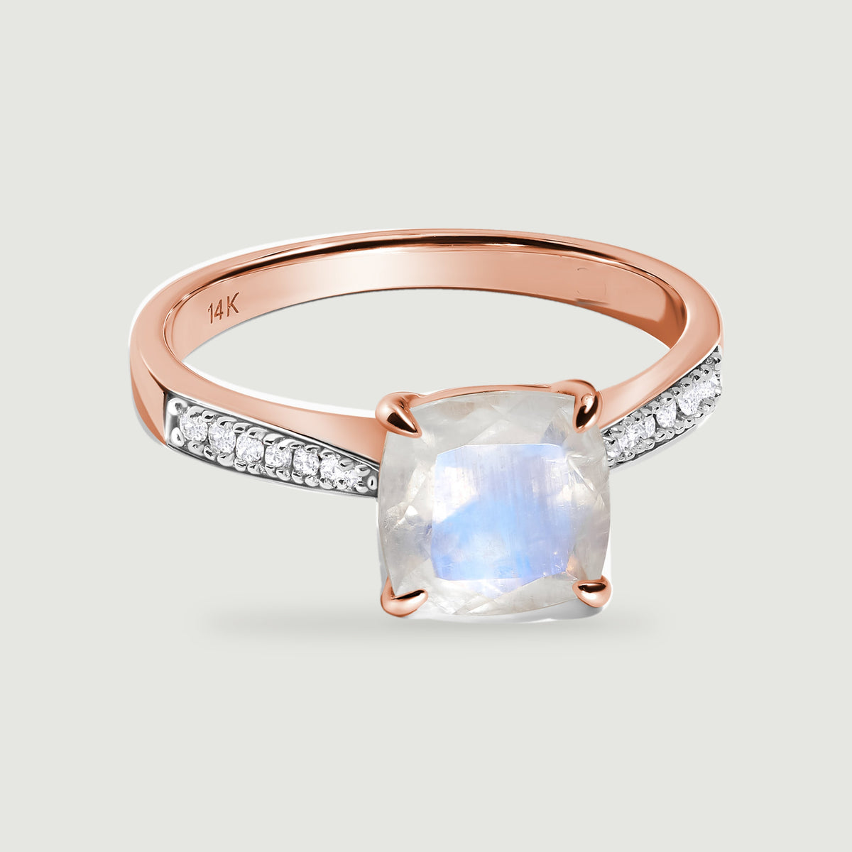 A rose gold ring displays a blue-flashing cushion moonstone between rows of small white diamonds.