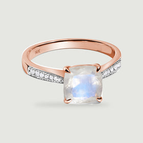 A rose gold ring displays a blue-flashing cushion moonstone between rows of small white diamonds.