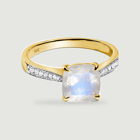 A yellow gold ring with four rounded prongs surrounds a pale moonstone above diamond-set shoulders.