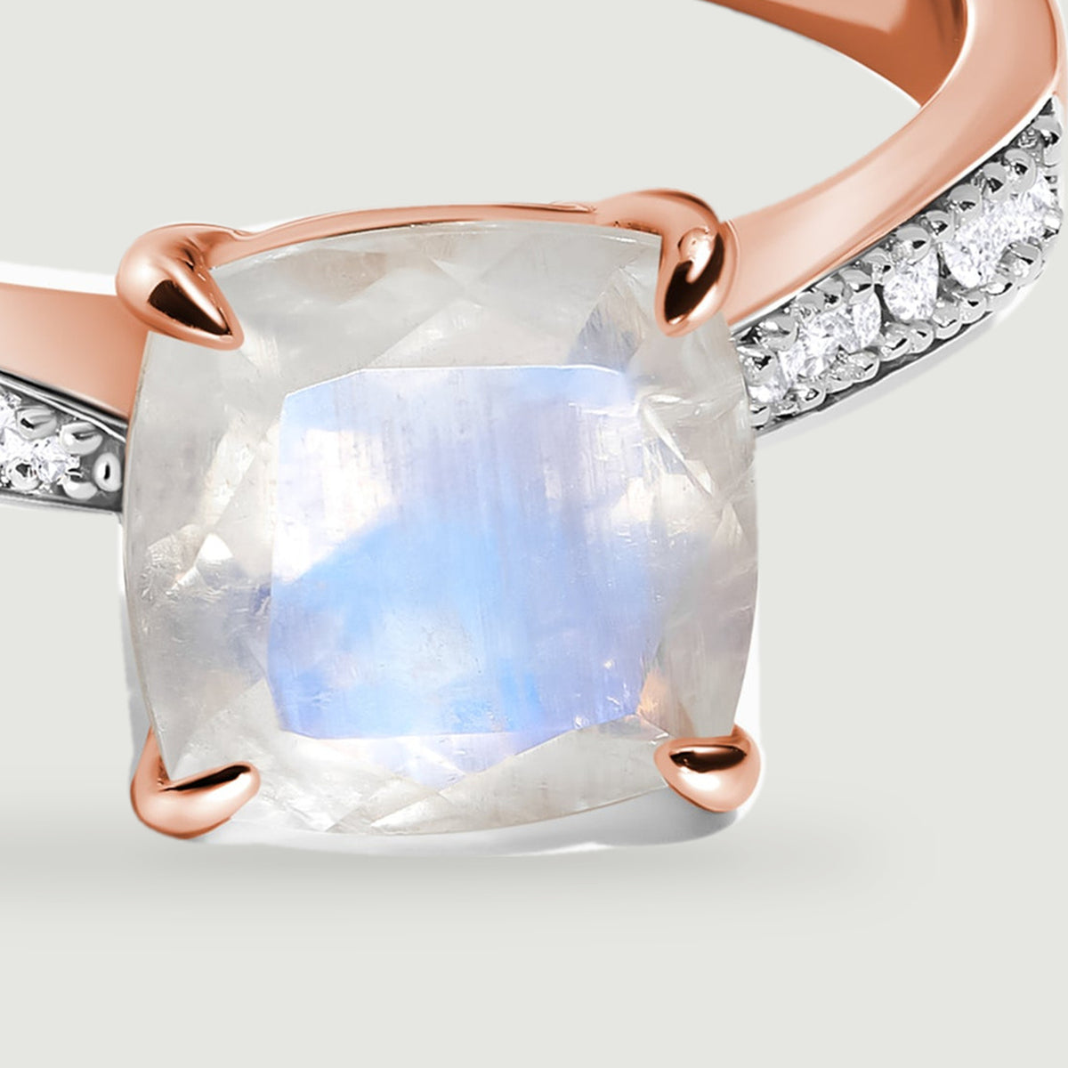 The rose gold prongs frame a cushion-shaped moonstone with a blue sheen beside small white diamonds.