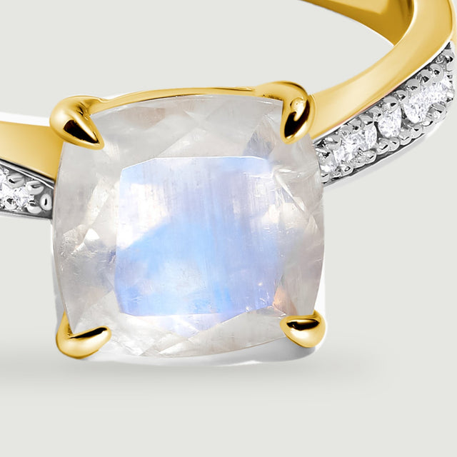 A close-up shows a blue-flashing moonstone held by yellow gold prongs above diamond-set shoulders.